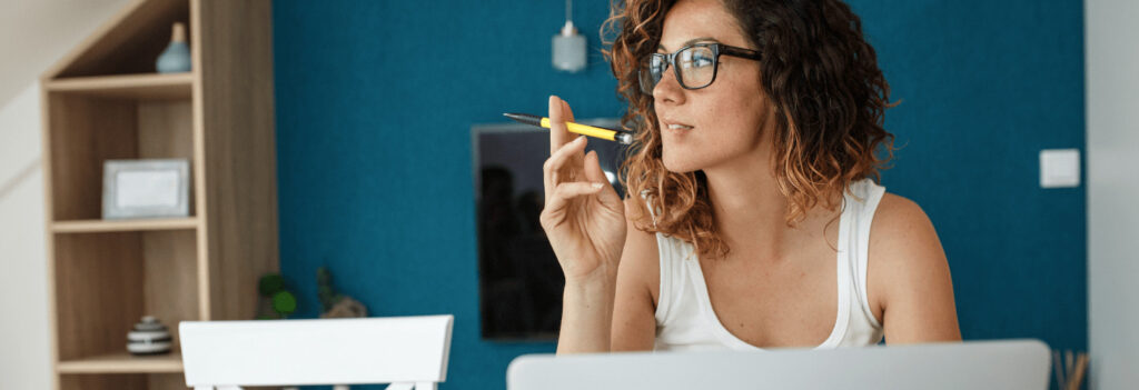 A woman holding a pencil and looking away from a computer, learning how to write a blog