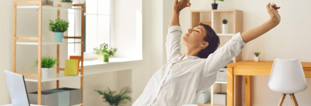 A woman at a computer desk stretching while taking a break to ward off mental fatigue