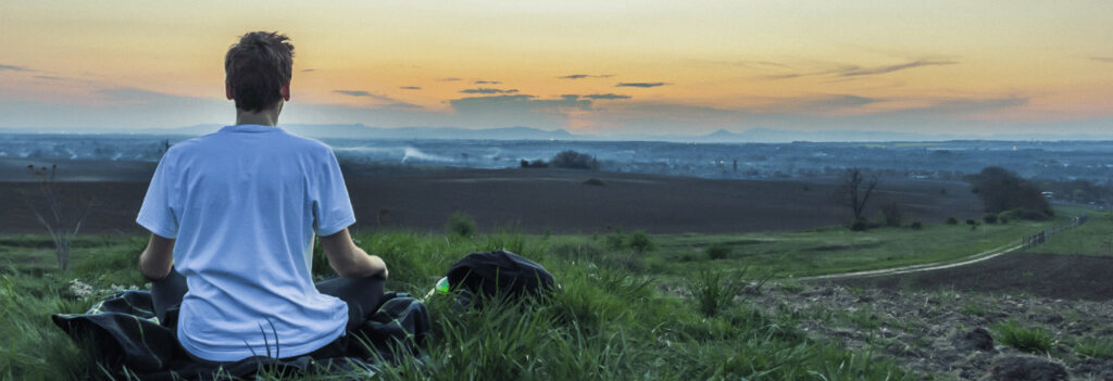 A man meditating in a field as a form of managing workplace anxiety