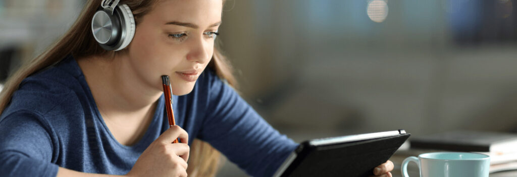 Young girl listening to headphones while holding a tablet, depicting aural learning styles