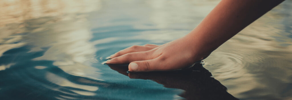 Hand touching a pool of water, making it ripple