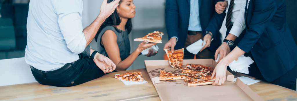 A group of employees sit around a desk together, eating pizza