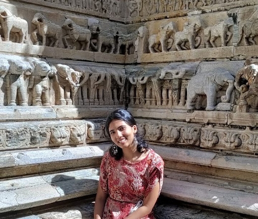 A woman sitting near carvings of elephants and other animals on a wall, smiling at the photographer